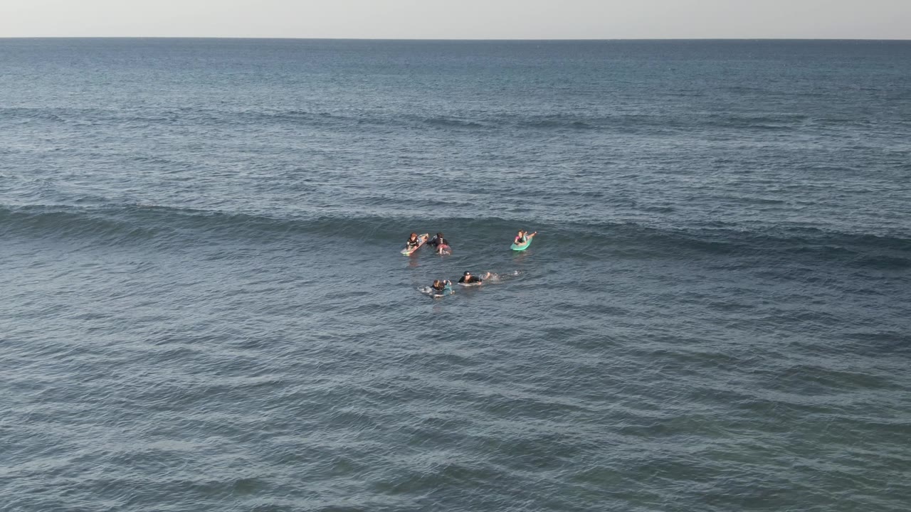 Surfers floating in open ocean with a darker swell line crossing the frame.