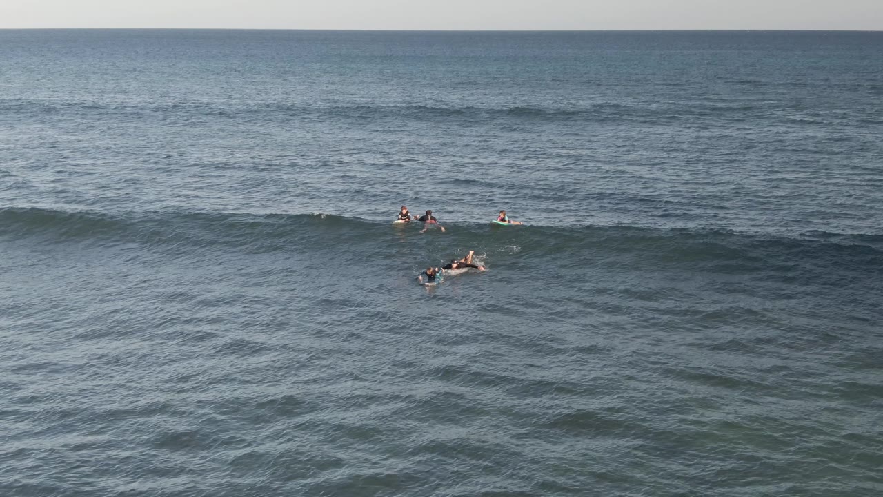 Wide Costa Azul Los Cabos surf lineup with several surfers and bodyboarders clustered near the crest area of a broad swell under clear daylight.