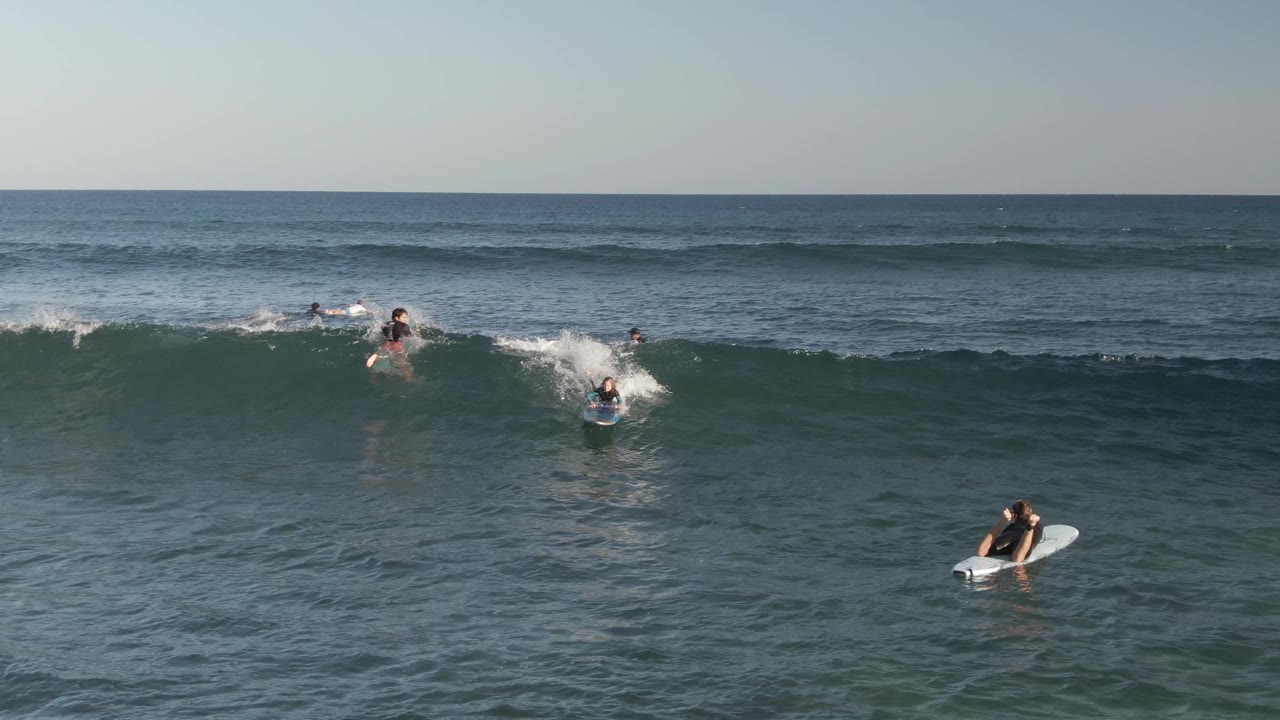 Aerial view at Costa Azul Los Cabos showing several visible surfers and bodyboarders paddling and waiting as a wave breaks across the midground.