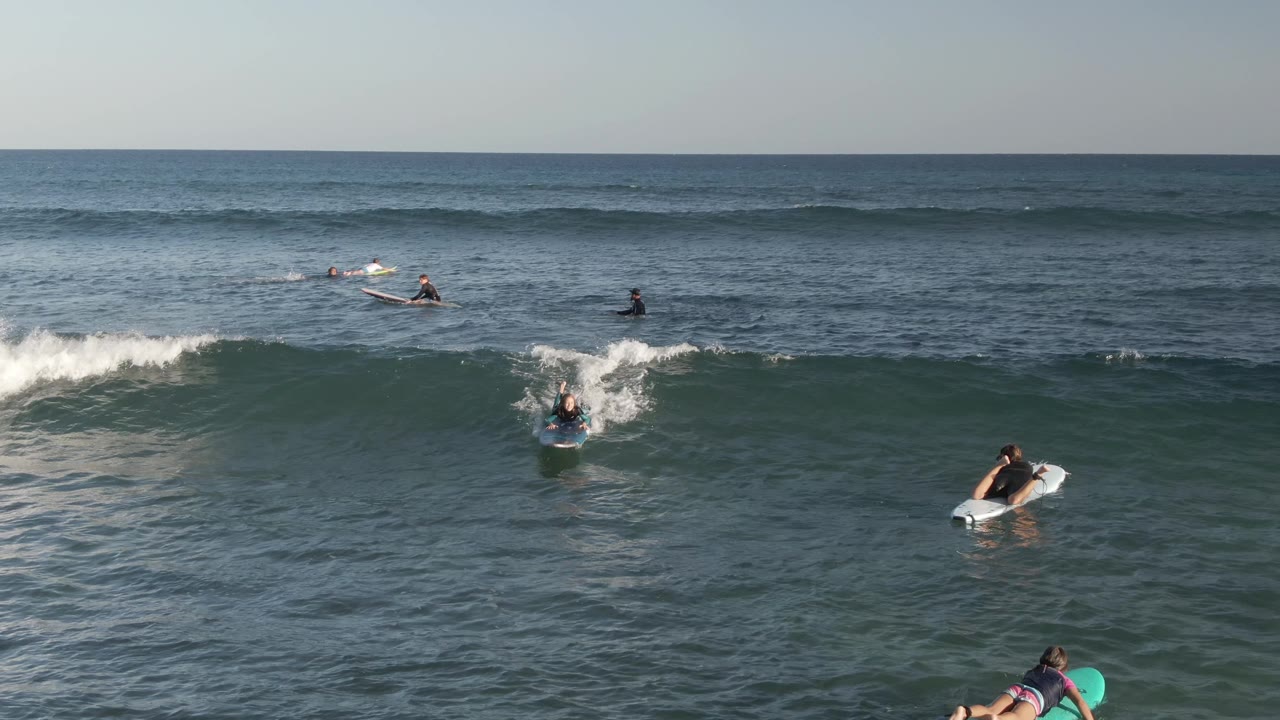 People on boards paddle near a rising ocean swell.