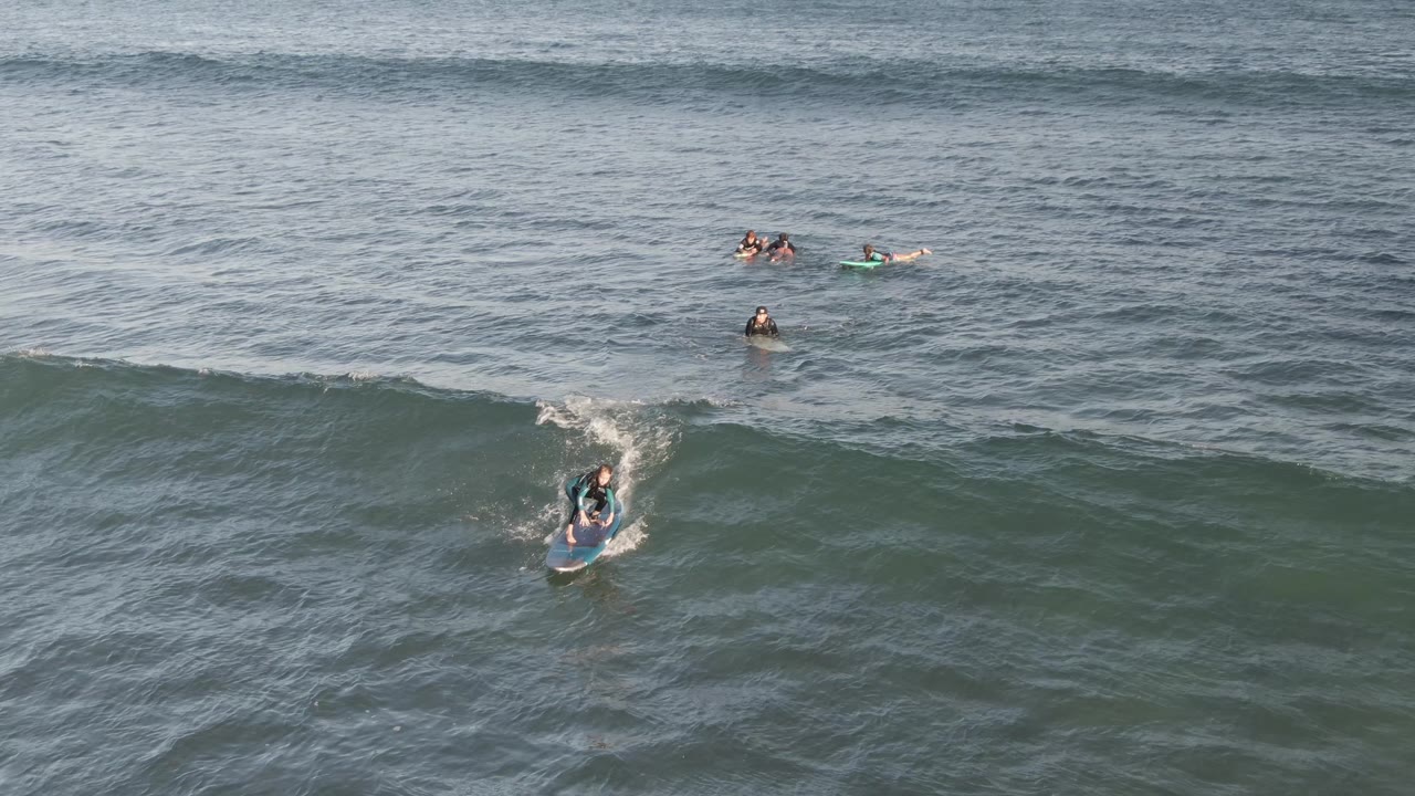 Aerial view at Costa Azul Los Cabos of a bodyboarder entering a green-blue wave while several distant swimmers and boarders wait farther out.