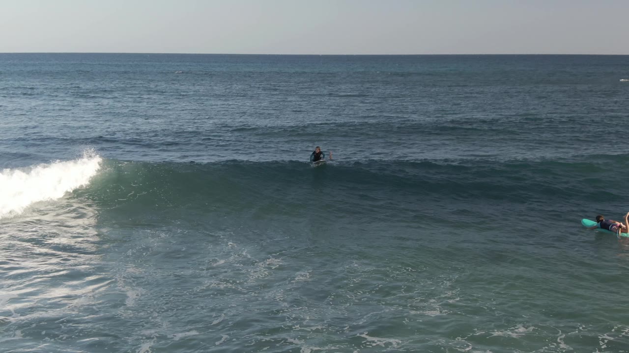 Whitewater rolls across a wave with surfers spread across the sea.
