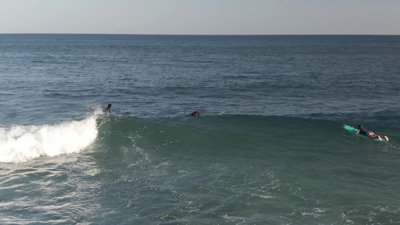 At Costa Azul Los Cabos, a bodyboarder with a bright board is close to the foamy crest while other surfers remain farther out in darker water.