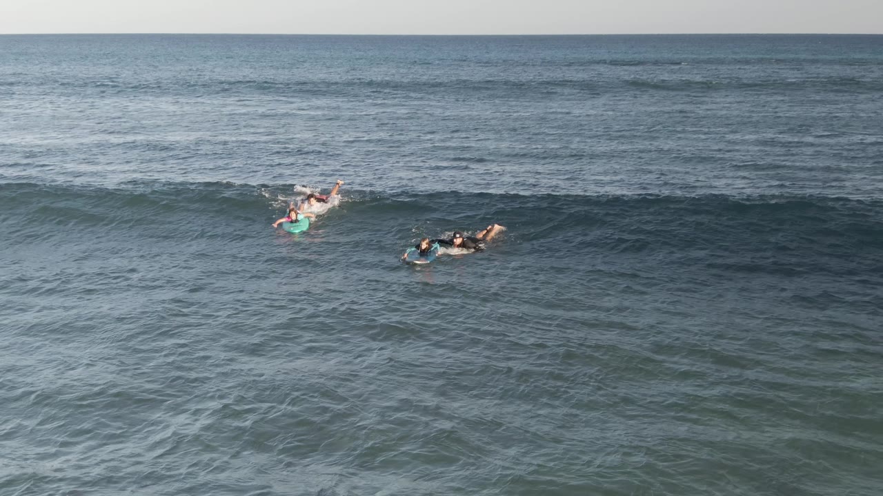 At Costa Azul Los Cabos, several people remain spaced along the face of a long rolling wave with open sea behind them.