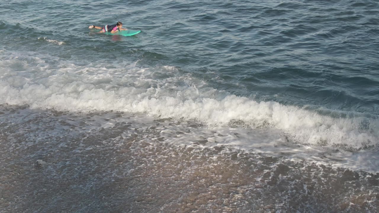 Bodyboarder paddling across blue water above a foamy shore break.