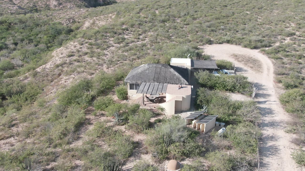 Round building and pale dirt road seen from above in a dry shrub landscape.