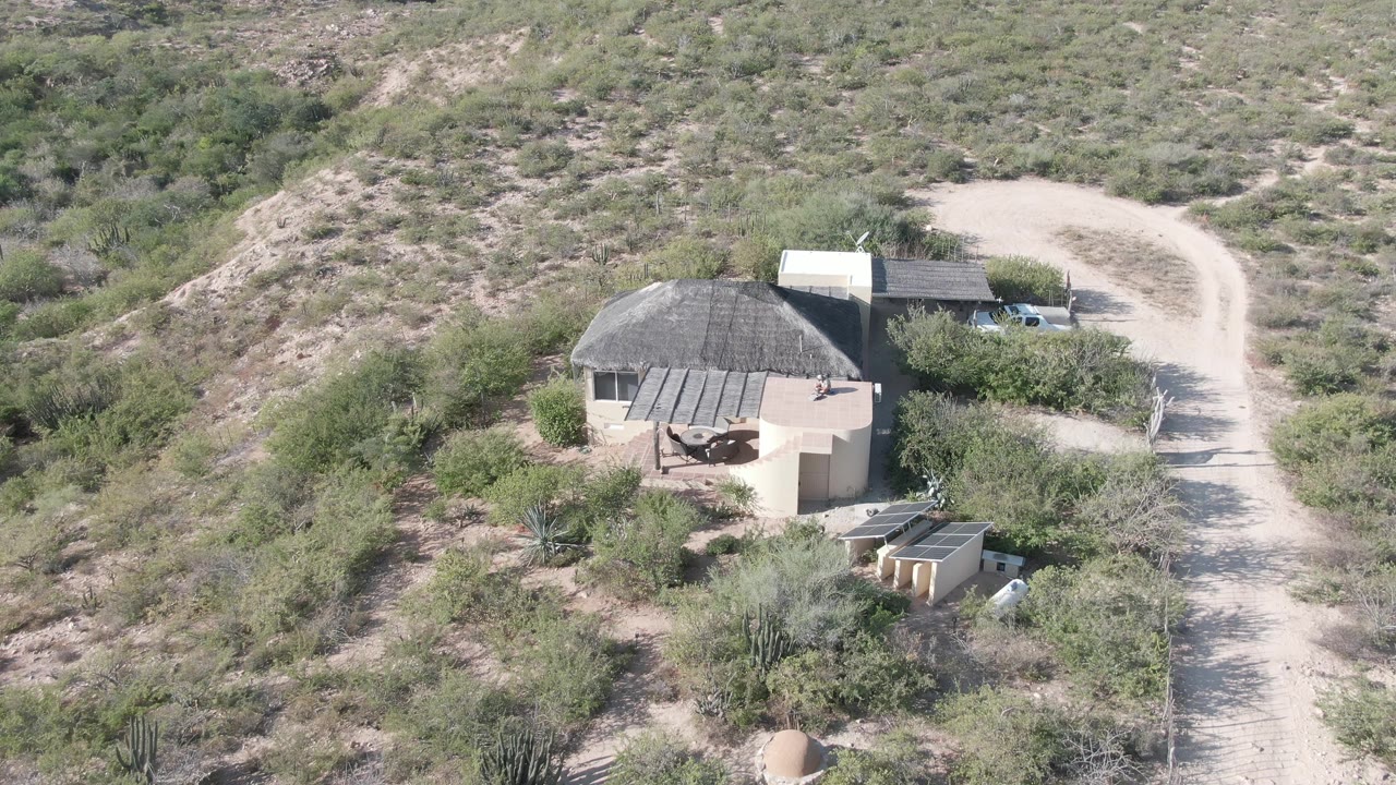 Cabo Pulmo aerial frame showing the round tan structure in the lower center, the dirt road on the right, a light-colored car near the road, and no visible people.