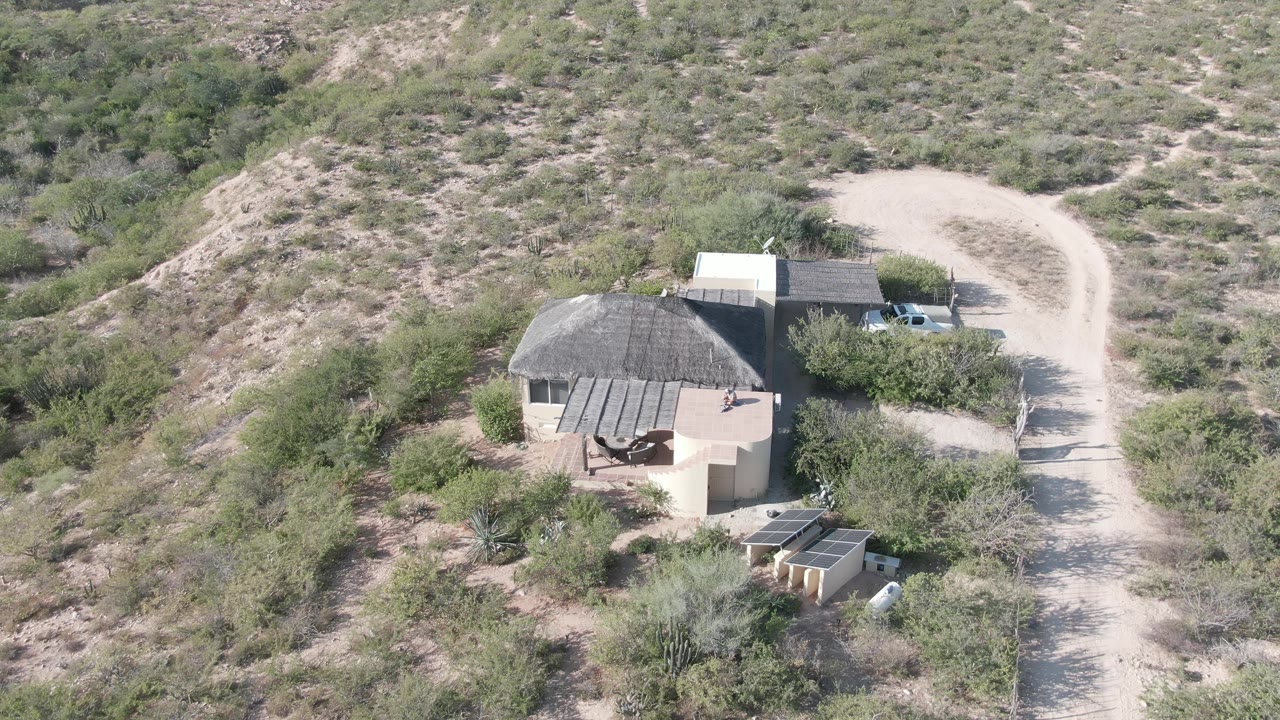 Aerial frame over a small house and curving dirt road in Cabo Pulmo, Baja California Sur, with a white truck near the structure and no visible people.