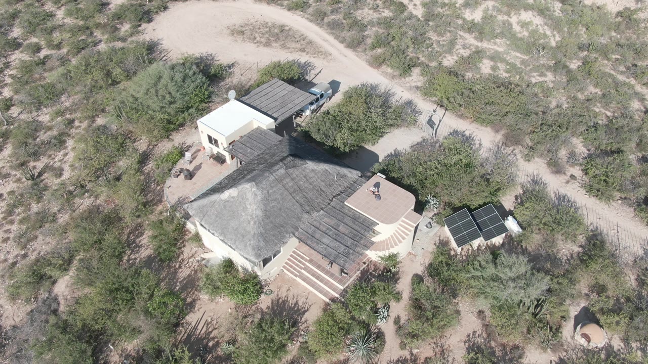 Drone view of a pale desert home, roof, solar panels, and surrounding scrub.