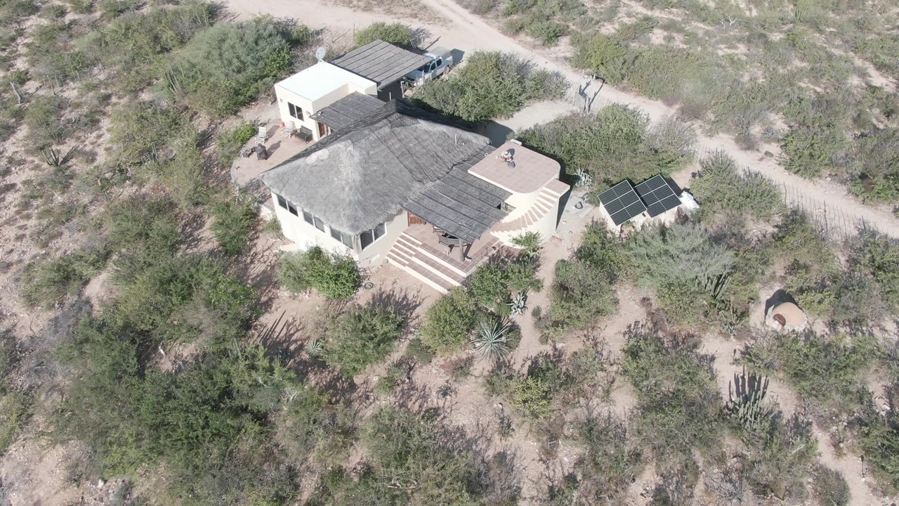 Aerial desert residence with cactus, shrubs, and solar panels nearby.