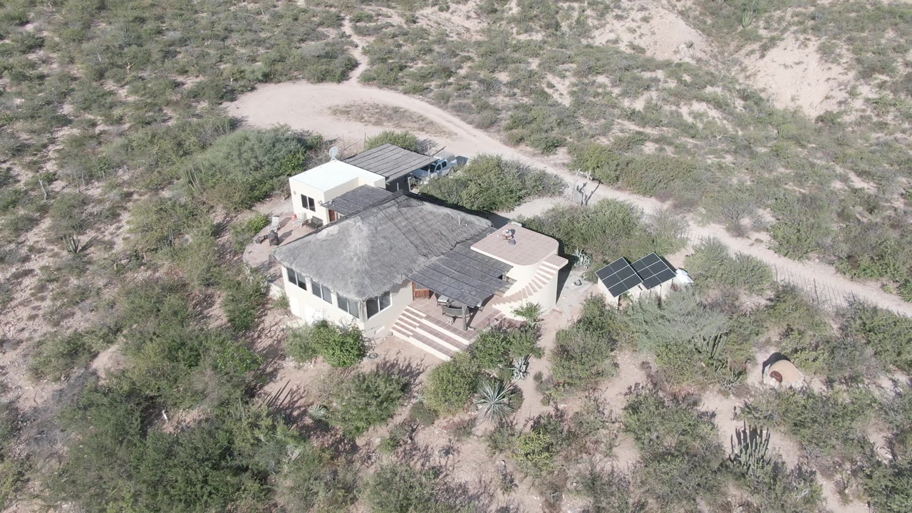 Desert house roof, steps, solar panels, and surrounding scrub seen from above.