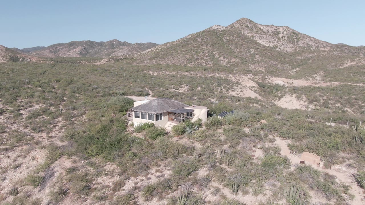 Desert house below a large rocky mountain under clear sky.
