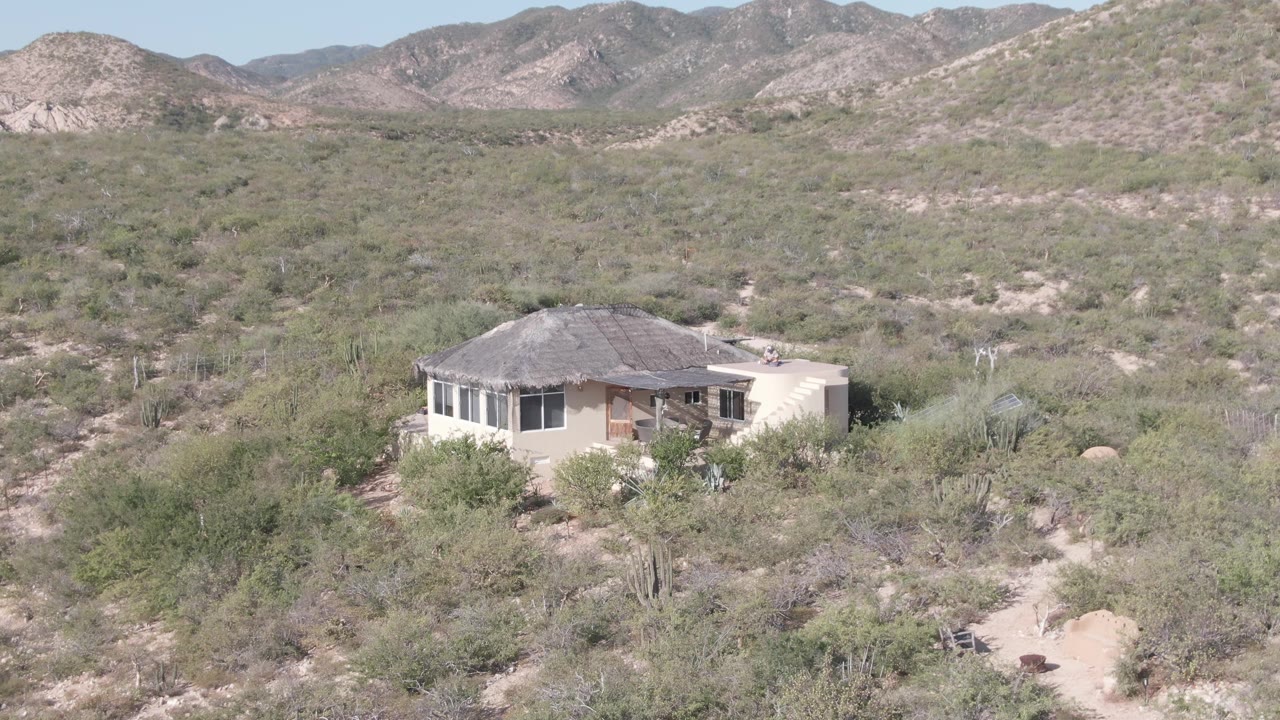 House at the edge of desert brush with mountains across the horizon.