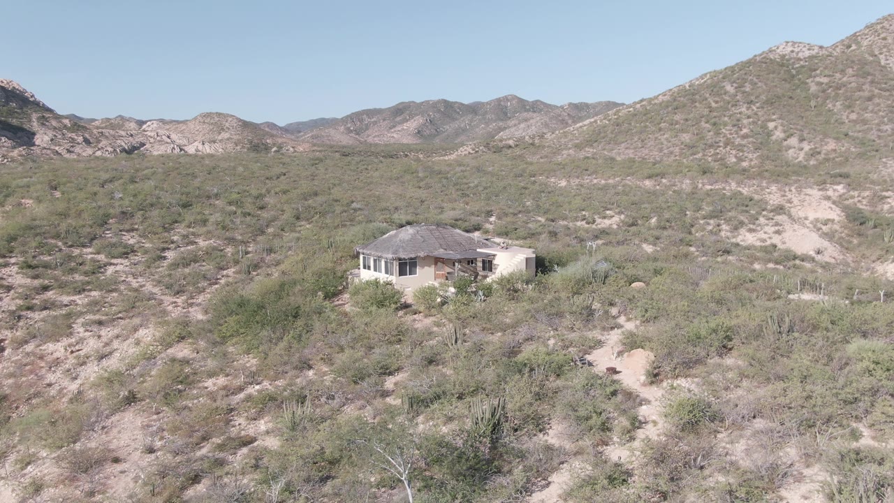 Desert house surrounded by brush with mountain ridge behind