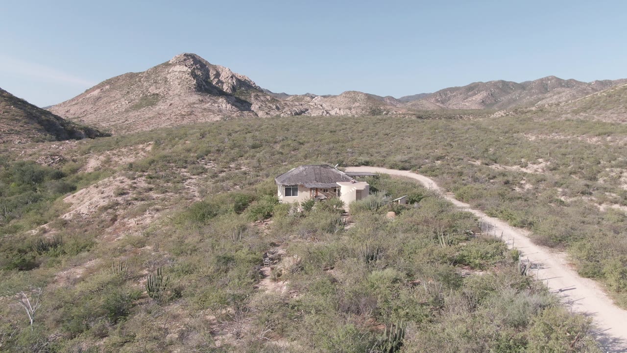 Desert road leading past a small building toward rocky mountains.