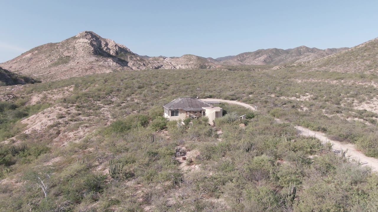 Desert house on hillside with road and mountains.