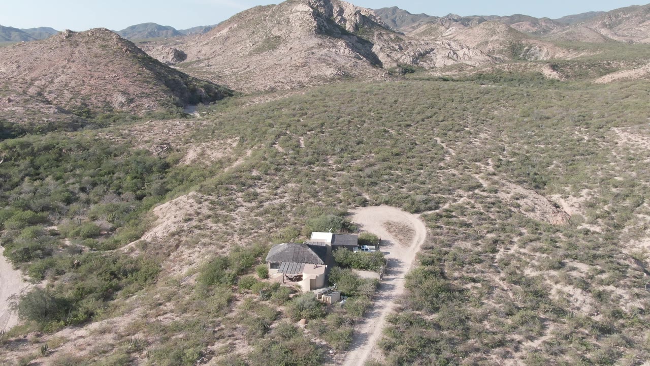 Aerial landscape with desert ridges, scrub, a pale road, and small structures.