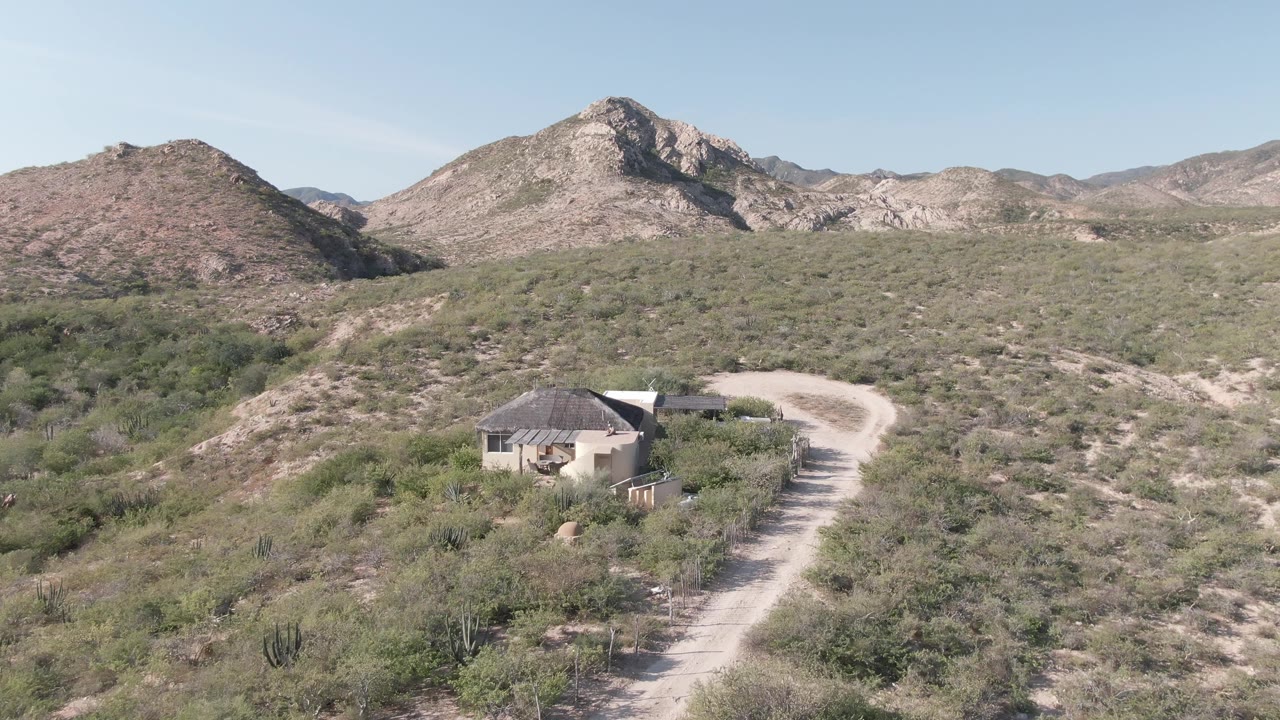 Third frame shows the Cabo Pulmo house lower in the scene, with the dirt road bending around the hill and a broad rocky mountain line beyond it, no visible people.