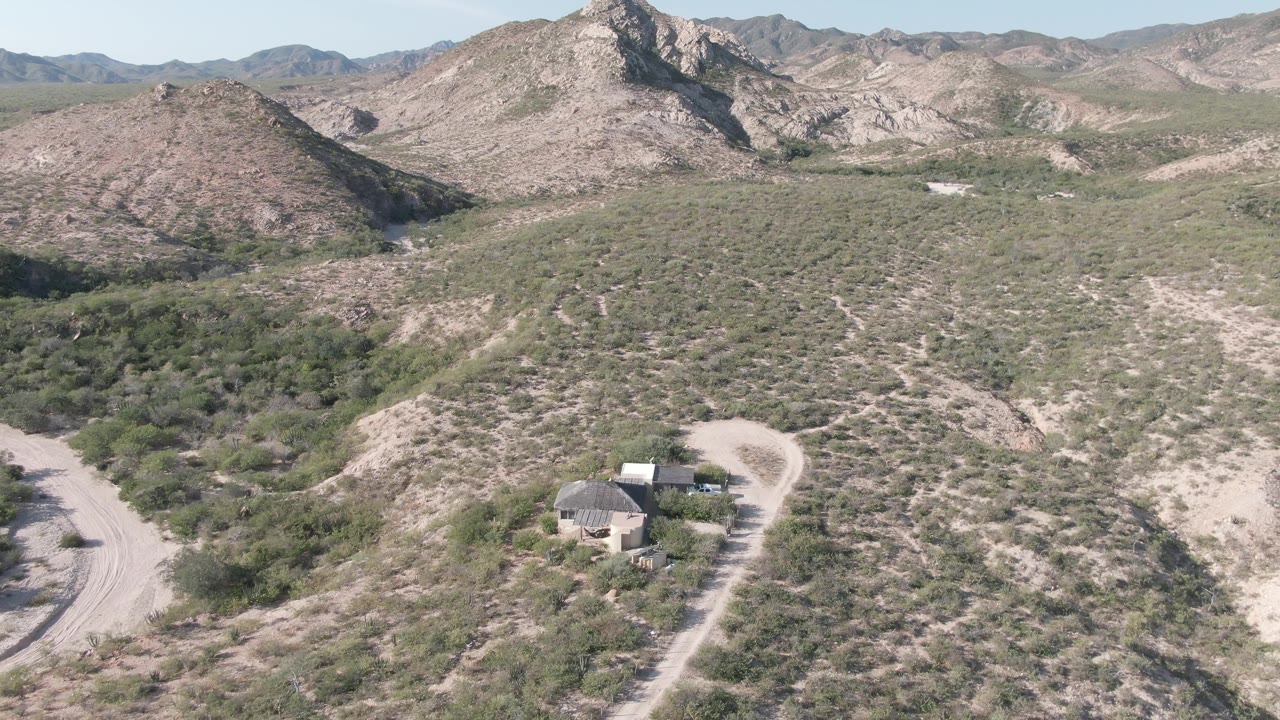 Aerial view in Cabo Pulmo, Baja California Sur, showing a small house beside pale dirt roads below rocky hills, with no visible people.