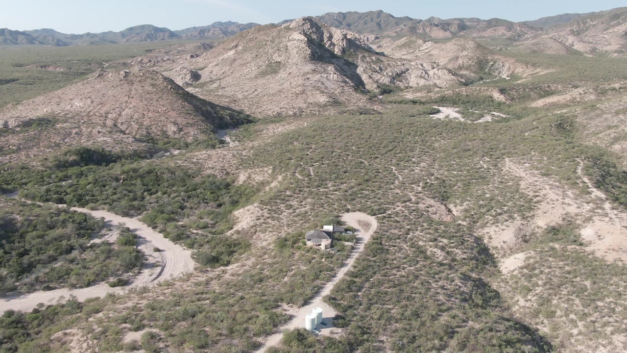 Aerial landscape with a dirt road bend, a white vehicle, scrub vegetation, and rocky mountains.