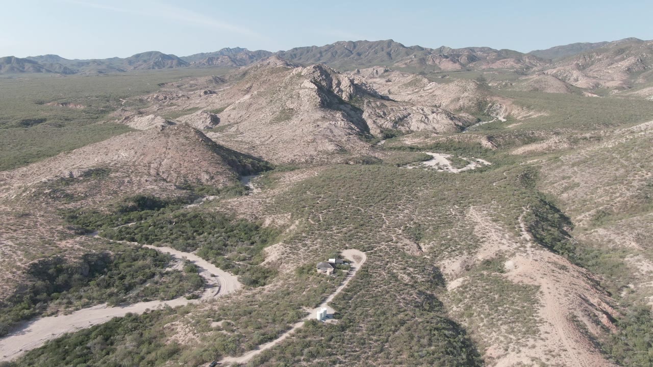 Wide aerial shot of a dirt road below rugged hills.
