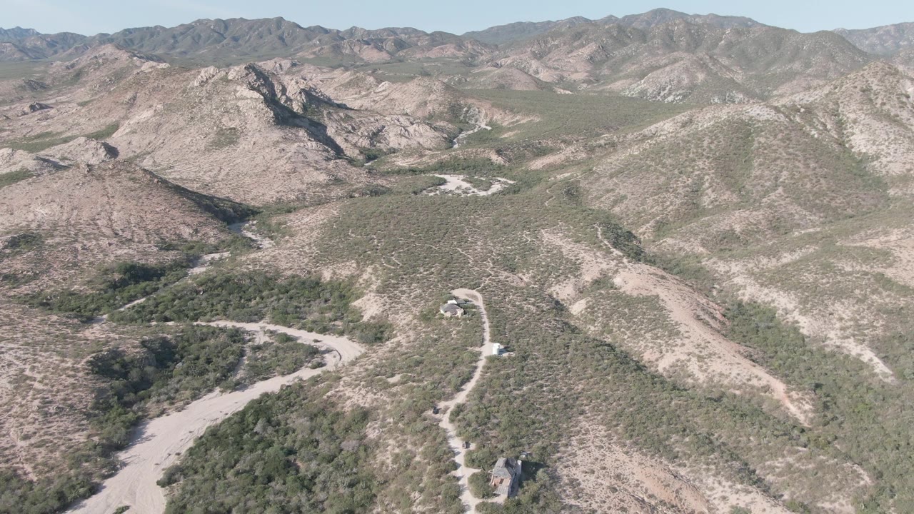 Cabo Pulmo aerial frame showing the road threading across a dry valley floor, green scrub patches on both sides, layered hills, and no visible people.