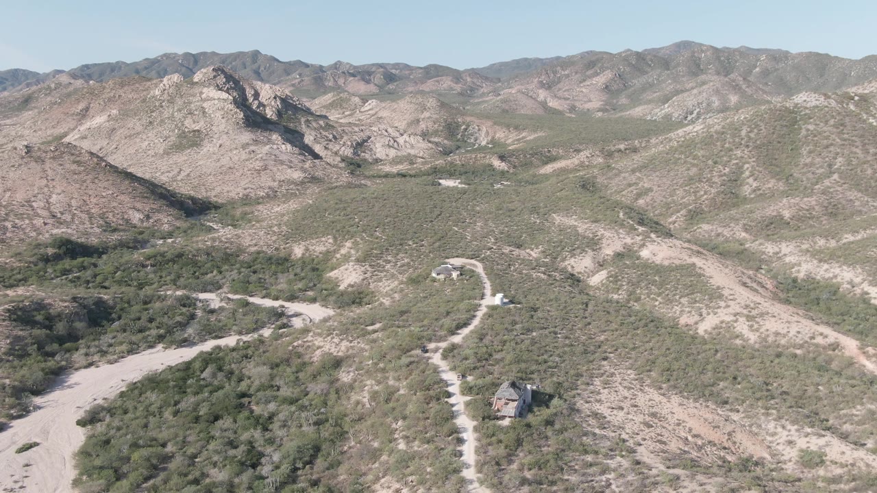 Aerial frame of desert hills with a pale road and small structure near the bottom