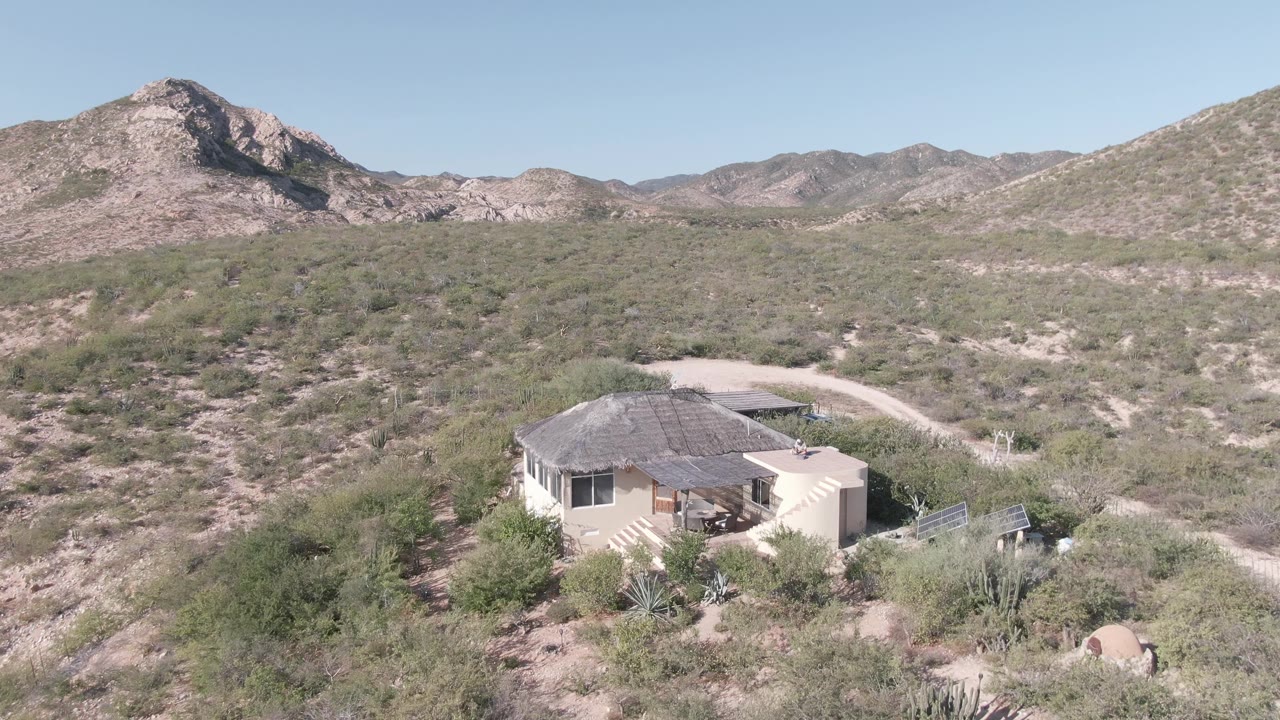 Aerial view of desert house with solar panels and mountain backdrop.