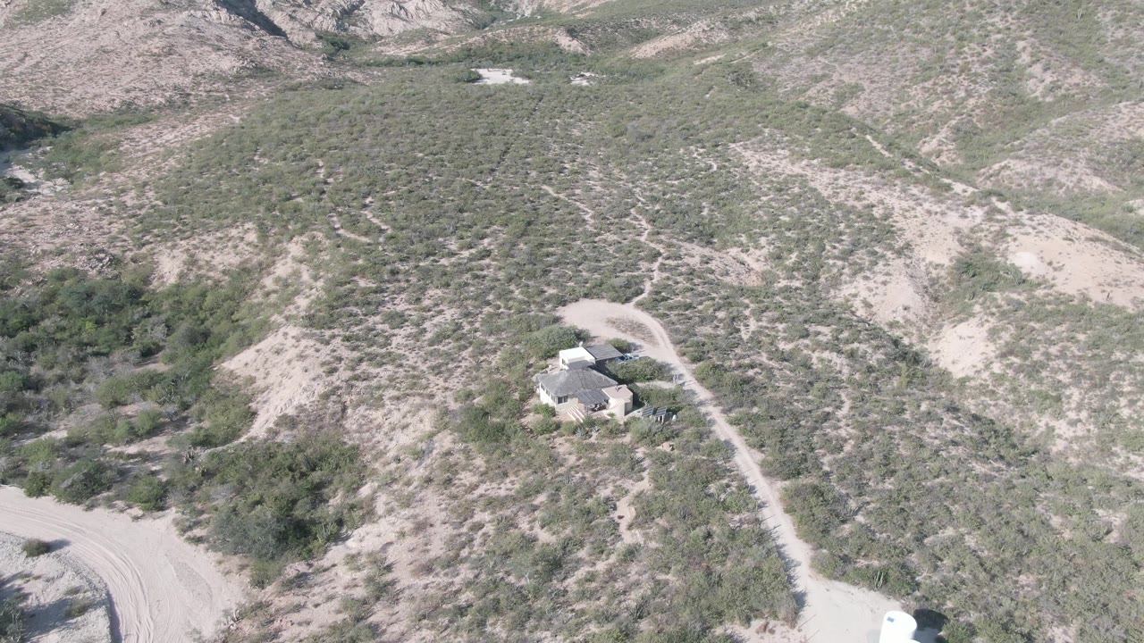 Aerial shot of an isolated house amid desert vegetation and a dirt road.
