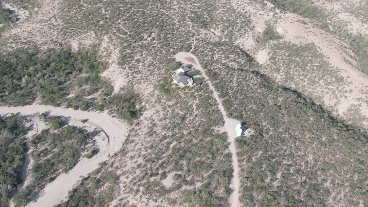 Cabo Pulmo aerial frame with a curved dirt road crossing scrubby hills and two small structures set apart from the main road, with no visible people.