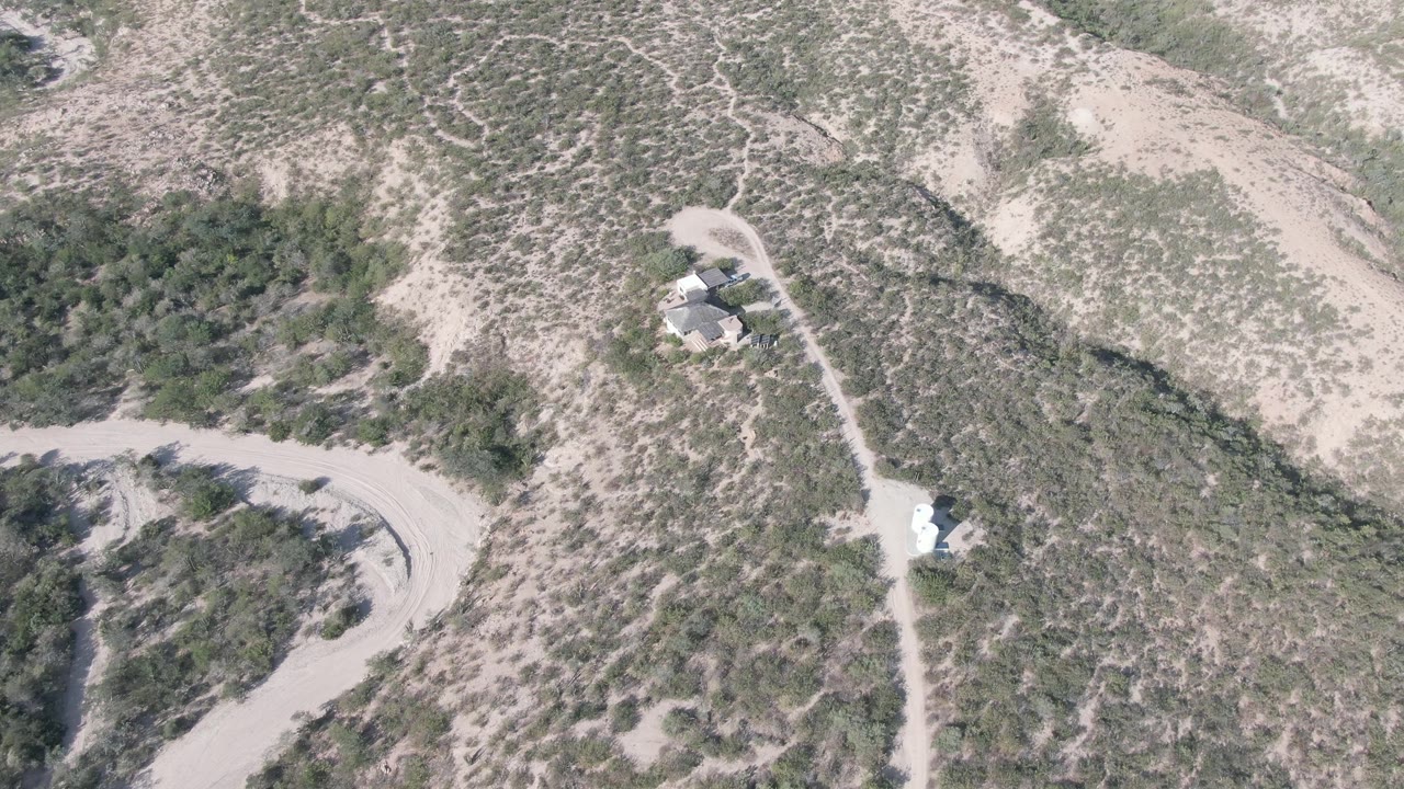 Overhead frame from Cabo Pulmo showing pale dirt tracks, patchy desert vegetation, and small structures near a narrow access road, with no visible people.