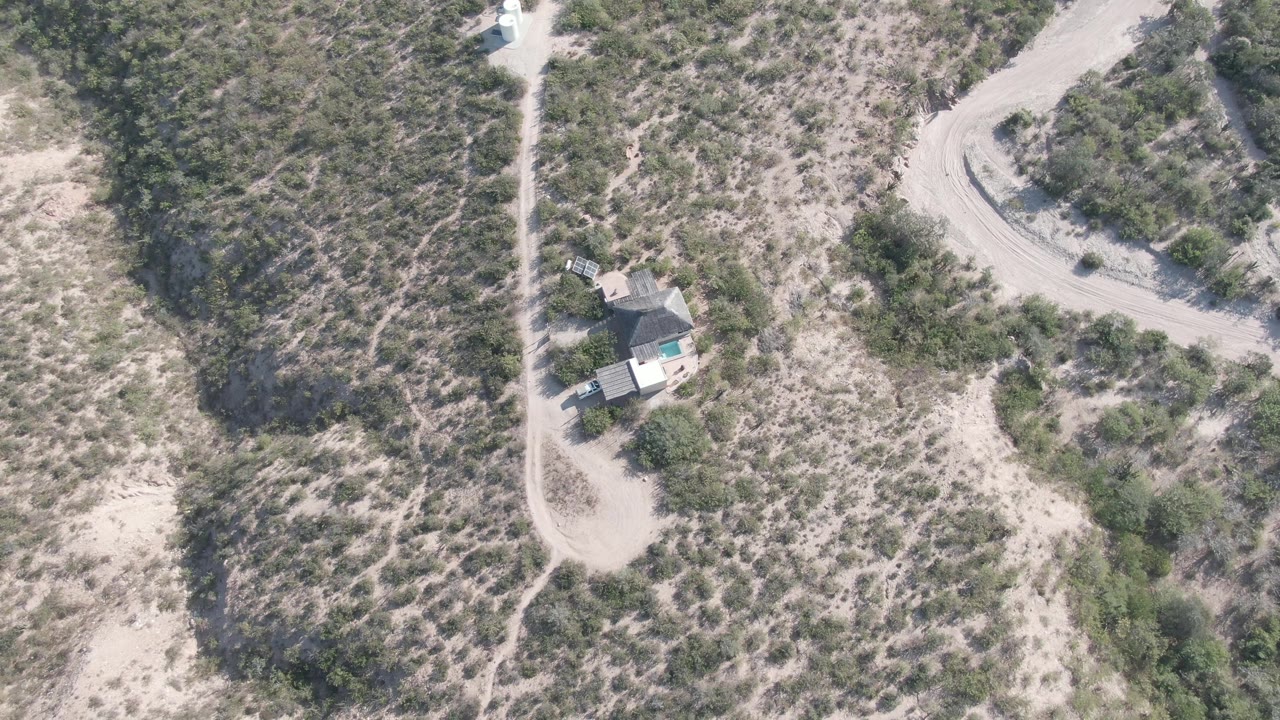 Second frame in Cabo Pulmo shows the vehicle slightly farther along the dirt path, with the small house below the track, scattered scrub, and no visible people.