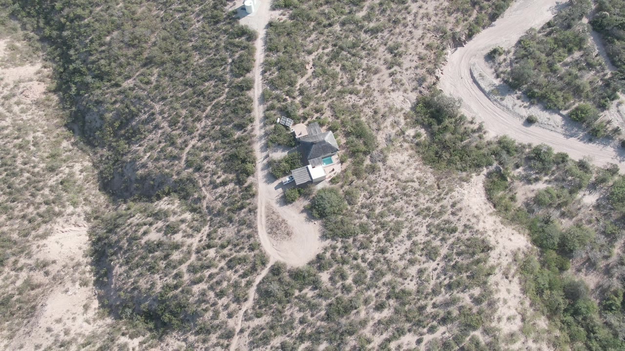 Mid-clip overhead view from Cabo Pulmo shows the vehicle along the dirt road, the small house offset below it, scrubby desert texture, and no visible people.