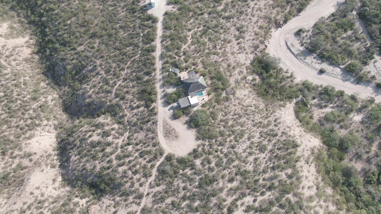 Aerial desert landscape with a vehicle on a pale road near a small house.