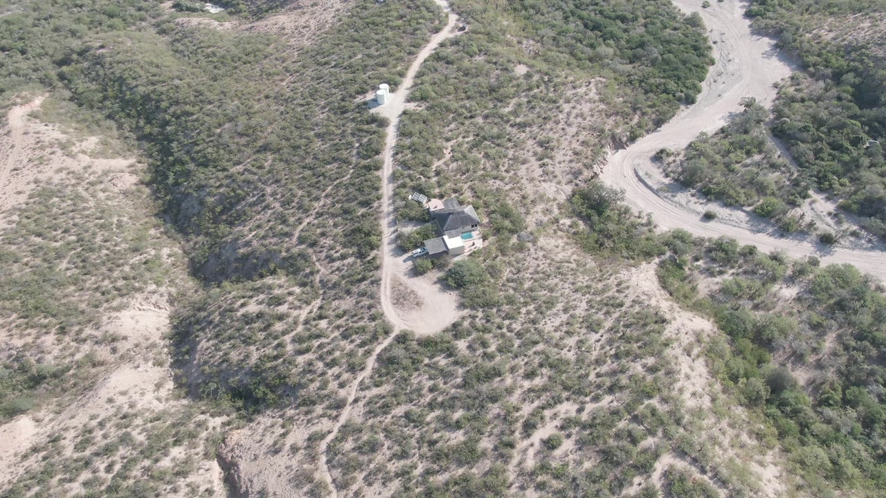 Aerial view of a hillside house below a dirt road curve.