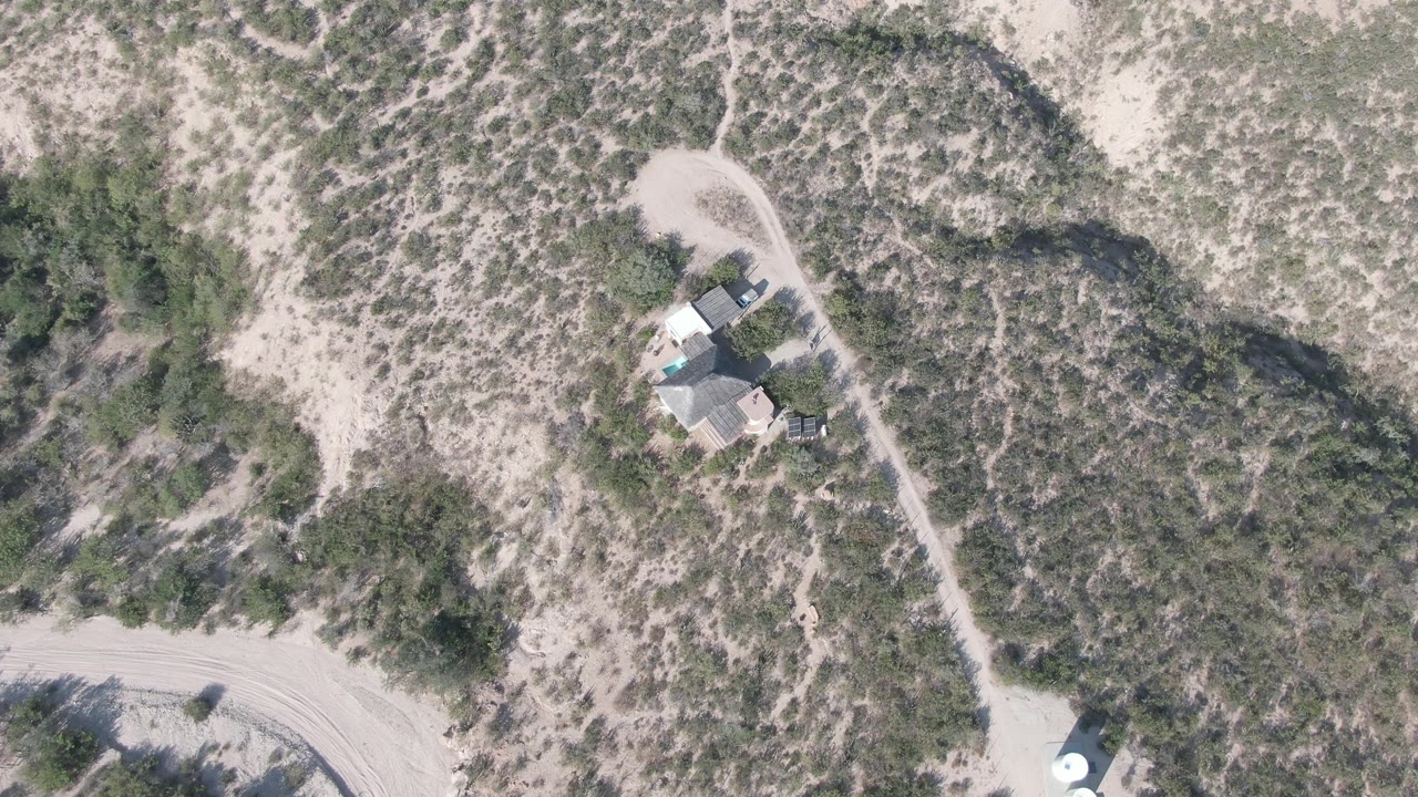 Aerial view in Cabo Pulmo showing the small structure slightly farther along the frame, with a curving pale road, patchy desert vegetation, and no visible people.