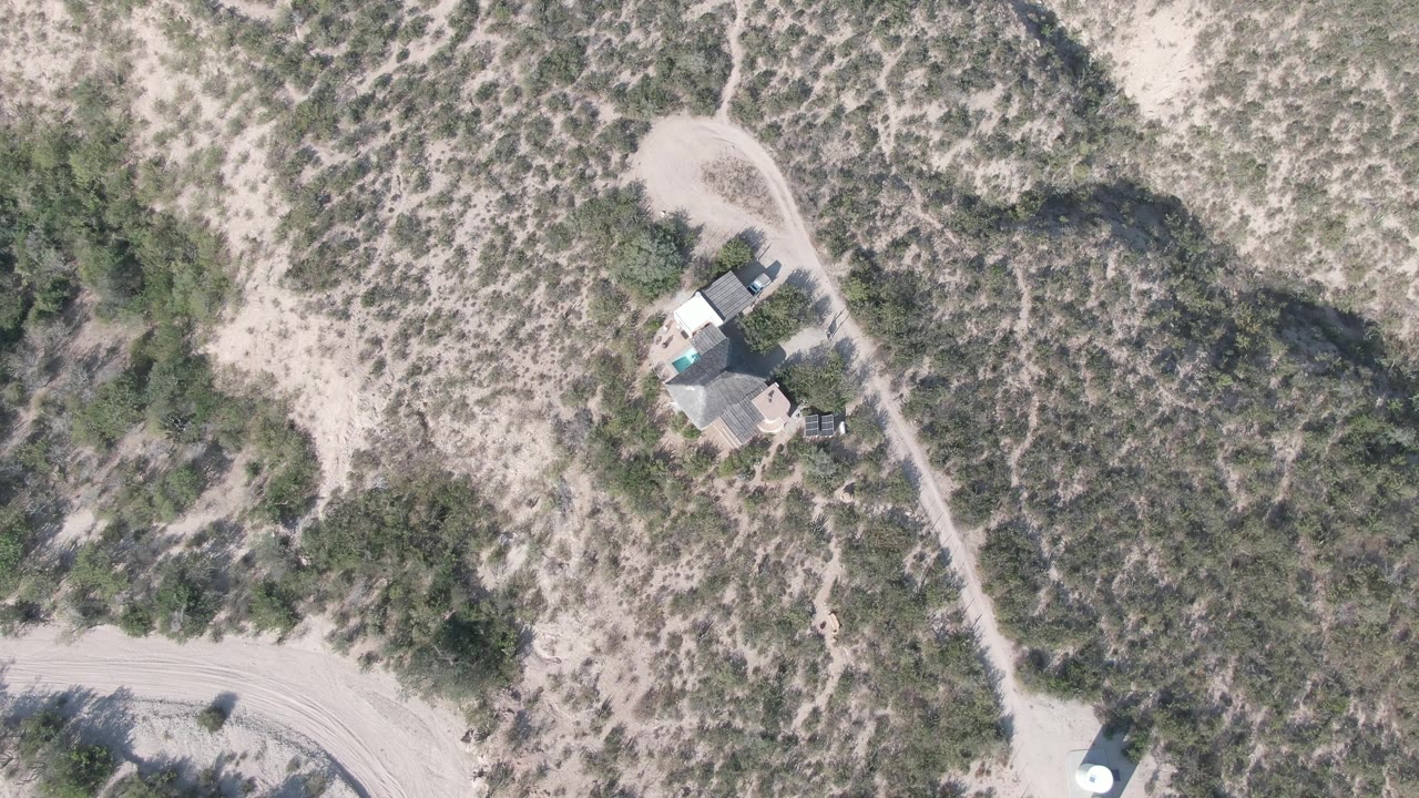 Aerial frame of a small desert structure near a sandy road.