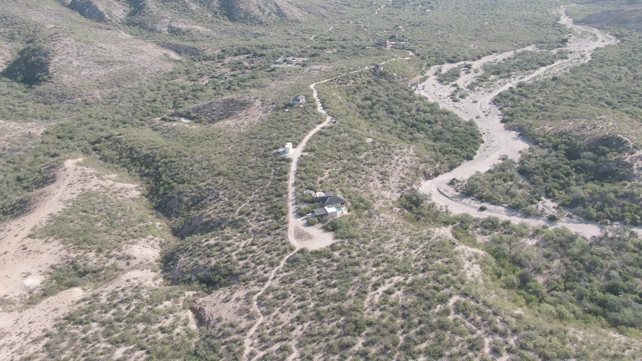 High aerial frame over Cabo Pulmo, Baja California Sur with branching dirt tracks, scrub-covered slopes, a small structure near the lower center, and no visible people.