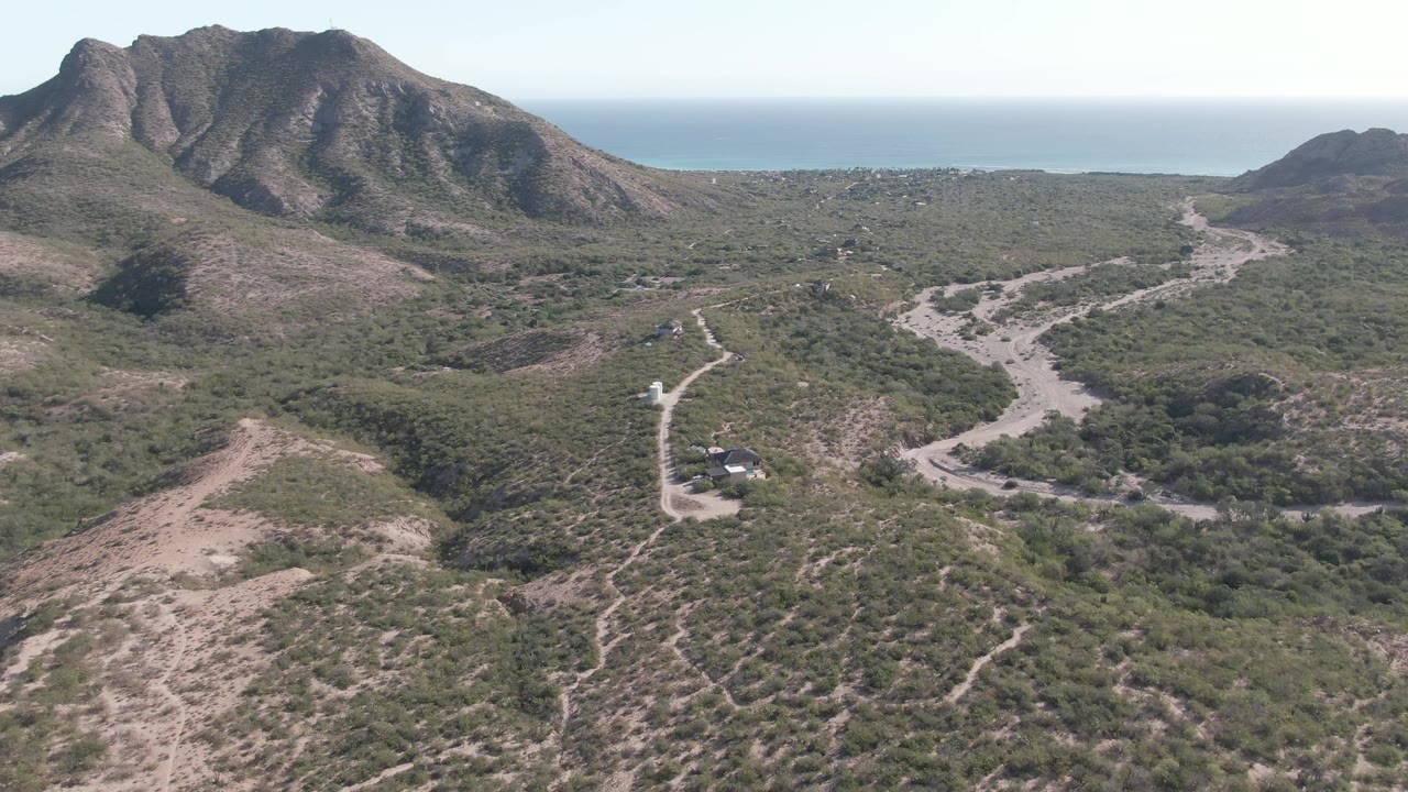 Aerial landscape with dirt road, vehicle, mountains, and distant sea