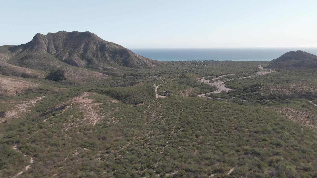 Coastal hillside aerial with mountain on left, road network, and ocean horizon.