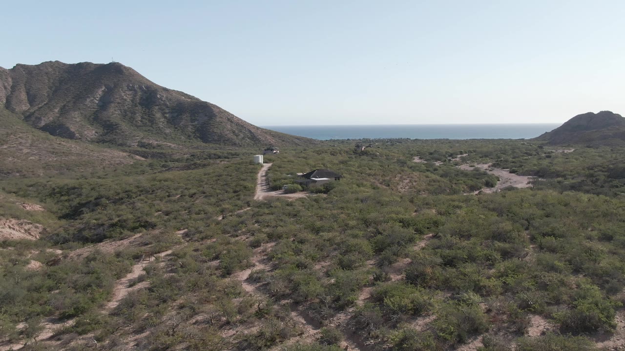 Aerial view of scrubland, dirt road, mountains, and distant ocean