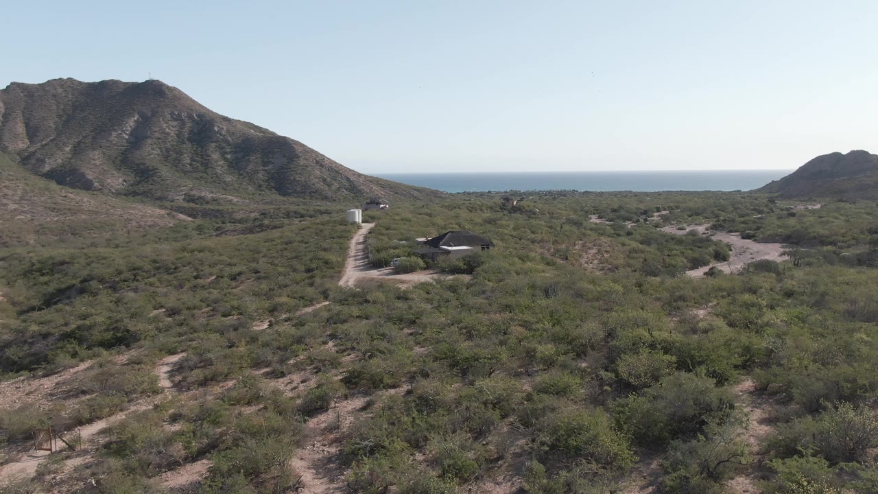 Cabo Pulmo aerial view with the mountain mass centered, low desert vegetation across the foreground, a road near the left side, ocean on the horizon, and no visible people.
