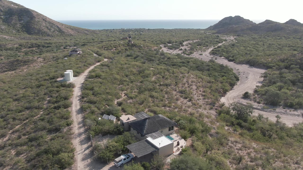 Drone view of a car leaving a house beside a winding dirt road.