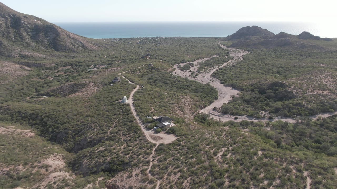 Aerial landscape with winding road, hills, small structures, and ocean