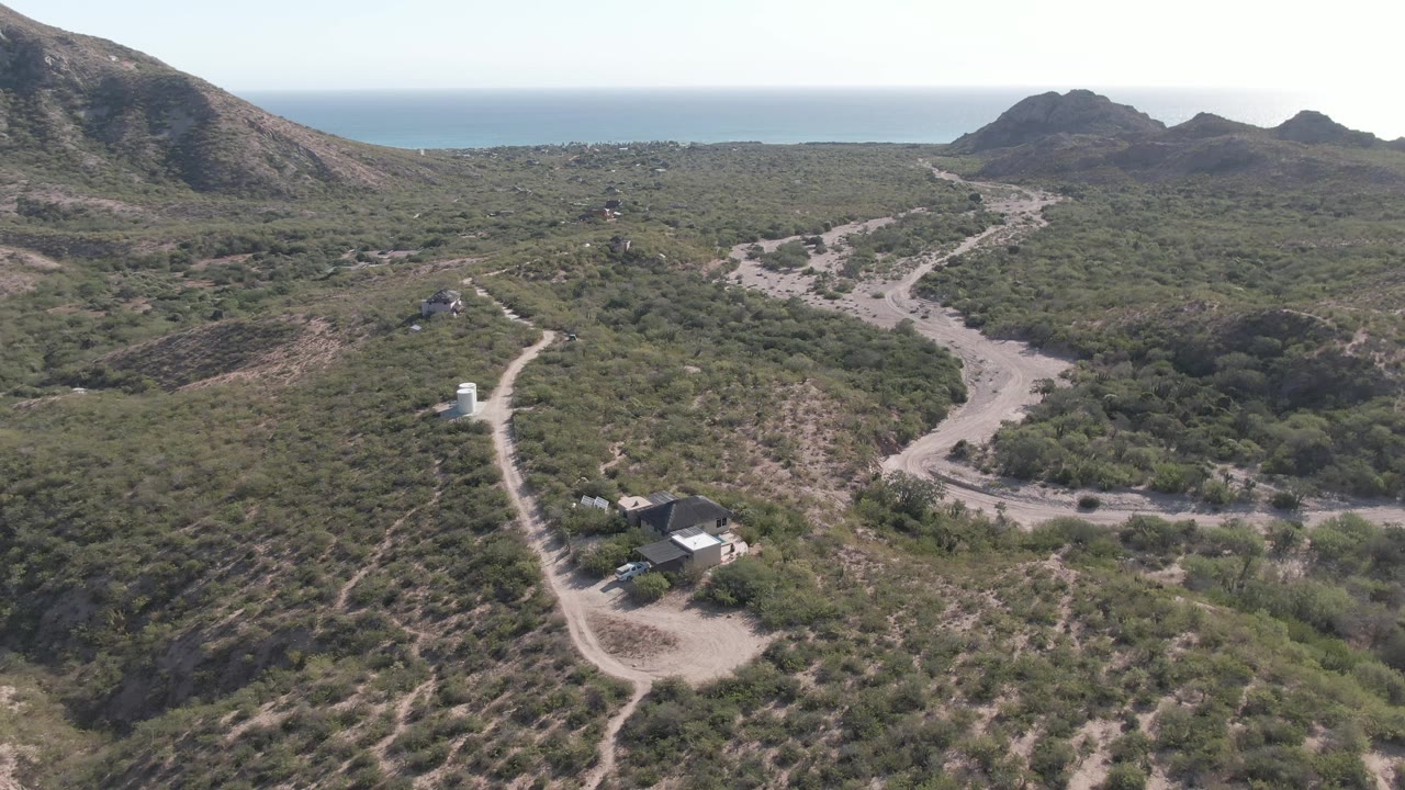 Aerial view looking across a dirt-road junction and coastal hills.