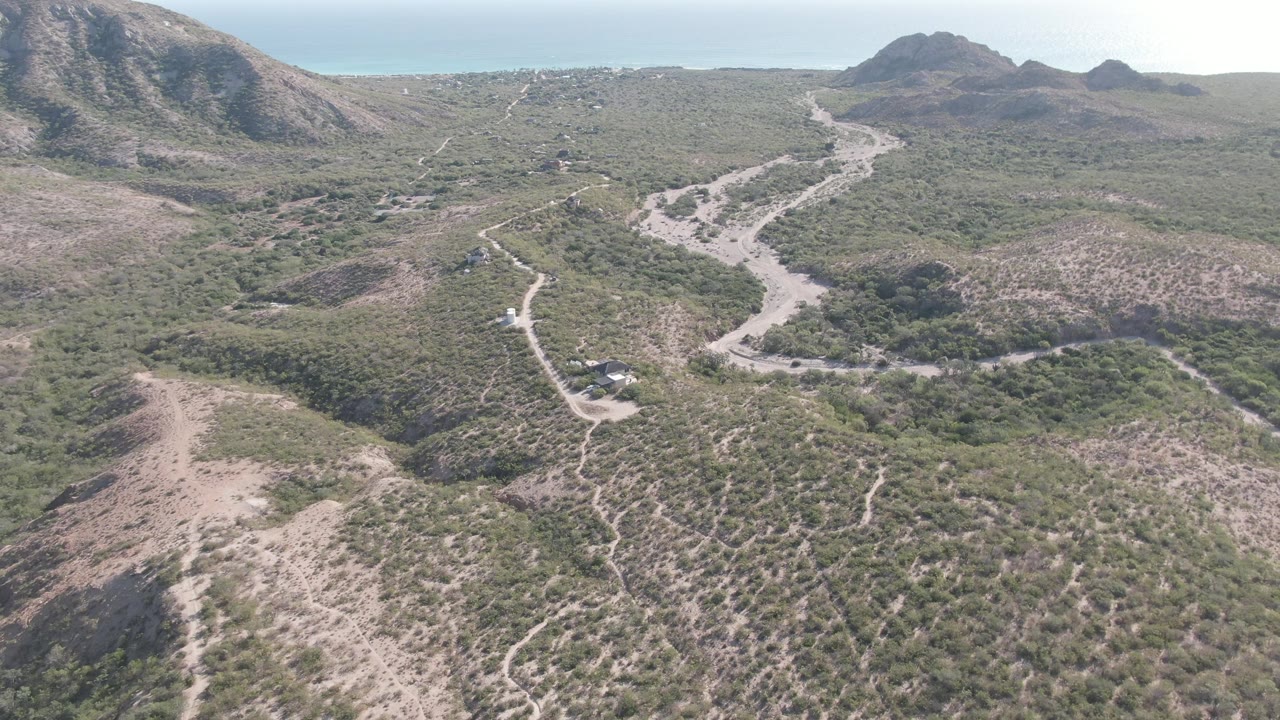 Aerial road view with scrub-covered ridges, a small vehicle, and mountains in the distance.