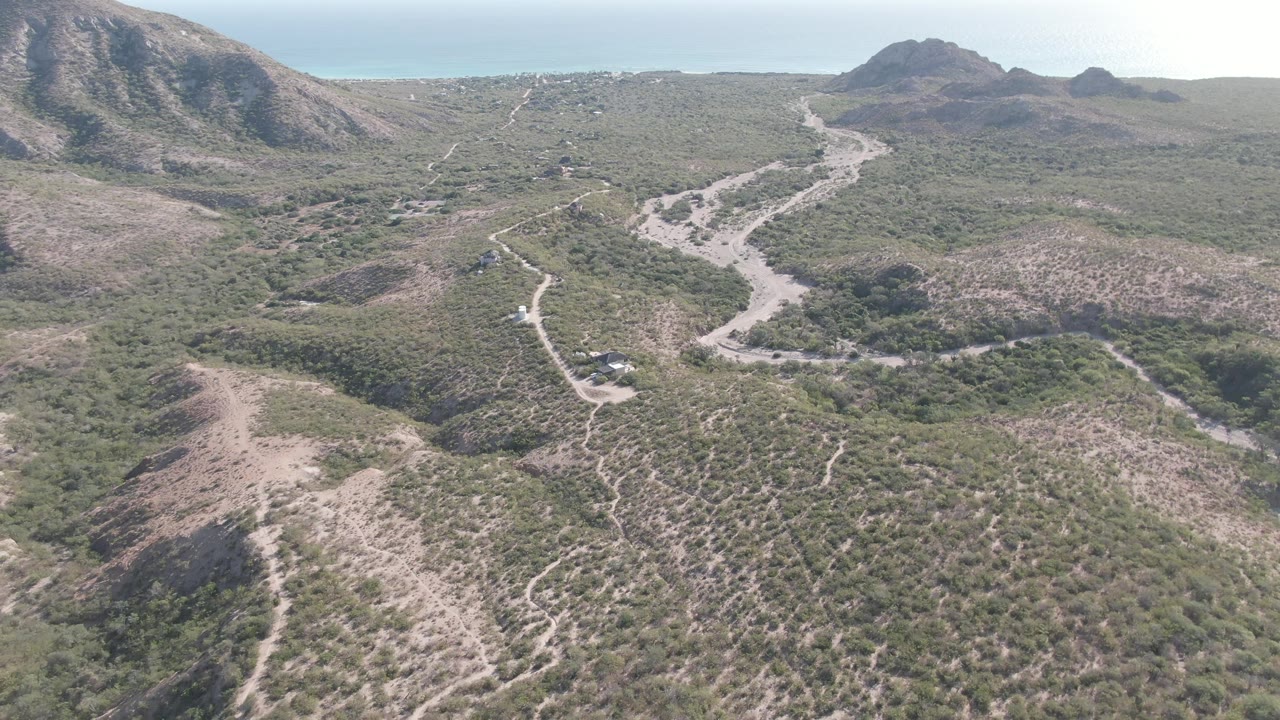 Drone view of a dirt track crossing green and brown desert scrub.