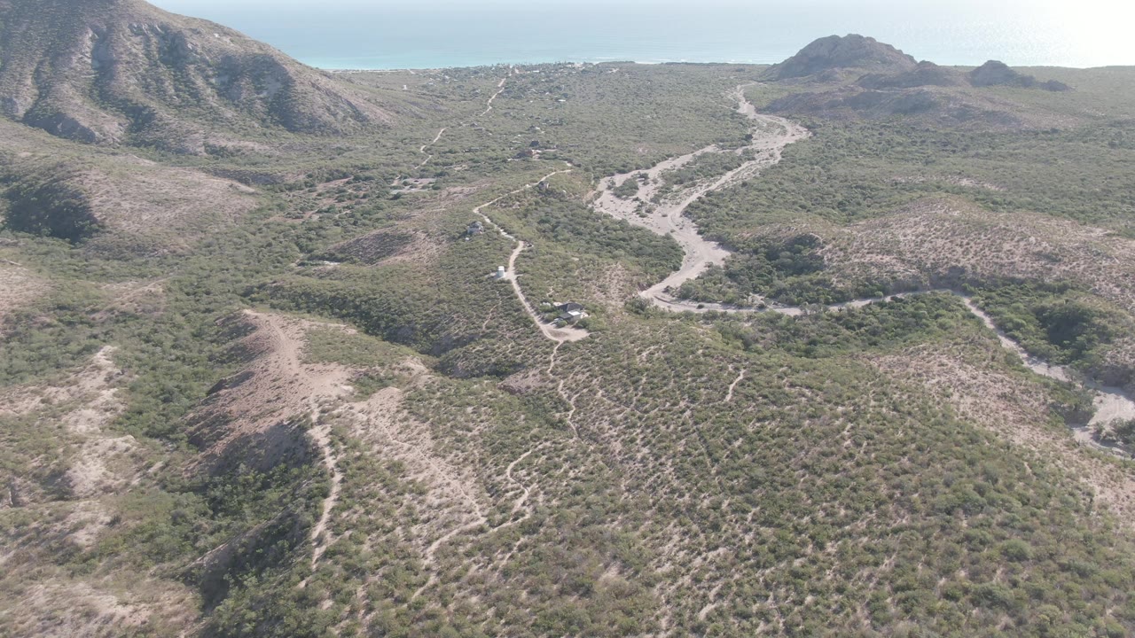 Aerial view of a vehicle on a winding dirt road through arid hills.