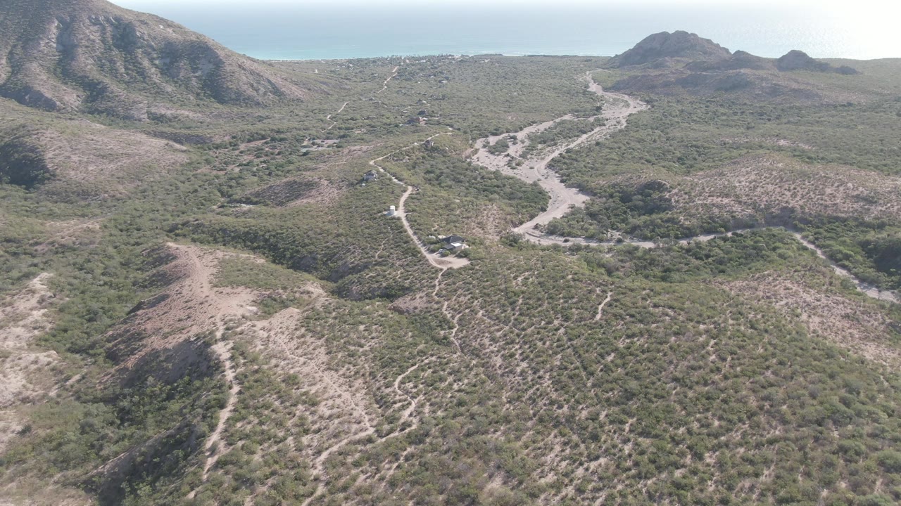 Aerial view over dry hills with a winding road and distant mountains.