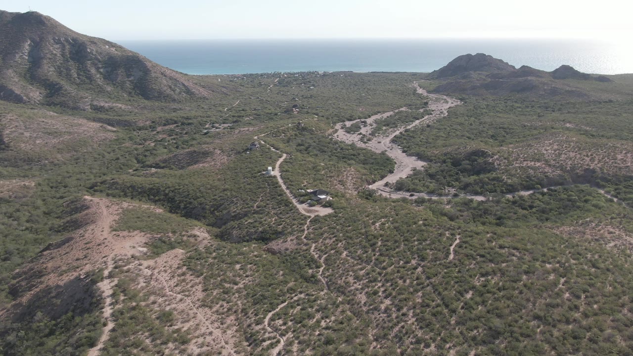 Second frame shows the Cabo Pulmo dirt road more centered in the valley, with scrubland spreading across the foreground, hills at both sides, ocean in back, and no visible people.
